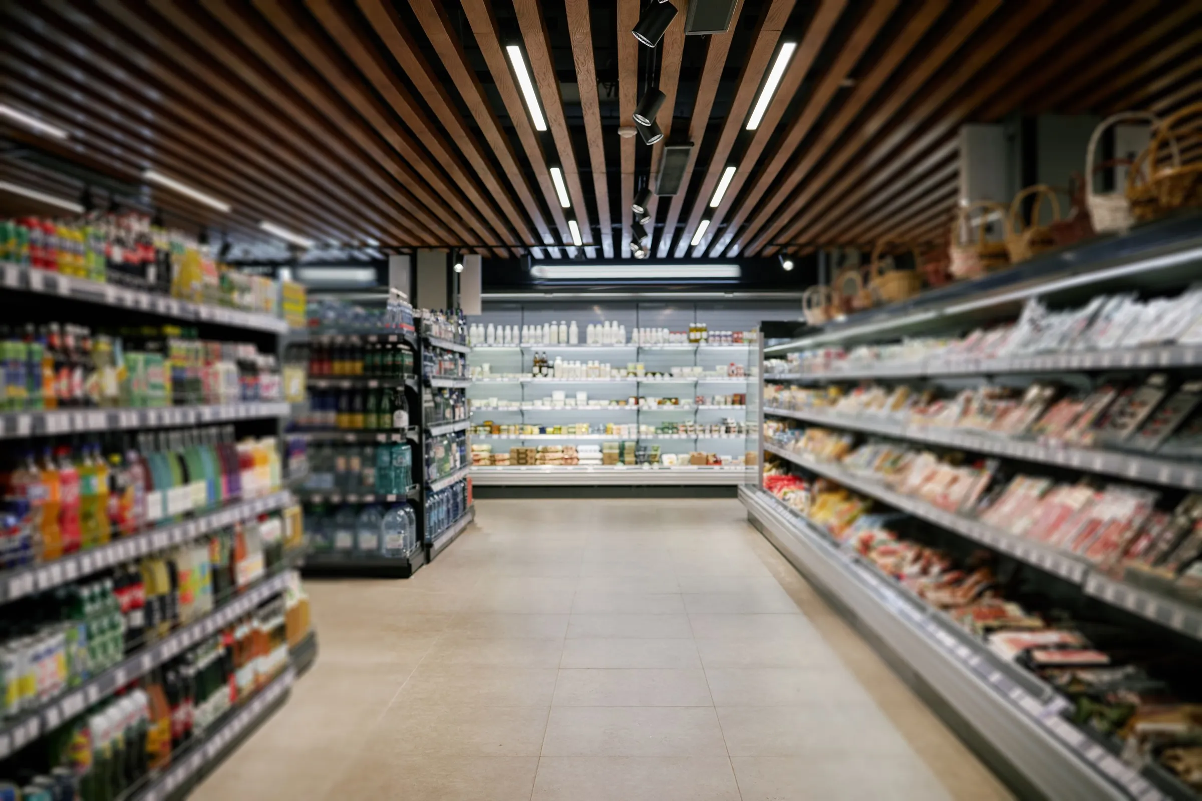 Long supermarket aisle with stocked shelves under a slatted ceiling